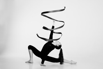 a girl from rhythmic gymnastics in a bodysuit rotates a ribbon sitting on a half-step