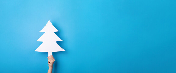 white christmas tree in hand over blue background, panoramic layout