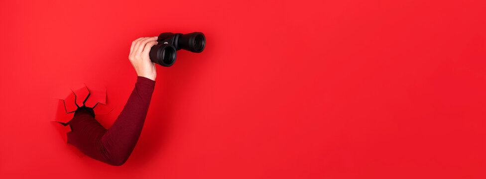 binoculars in hand over red background, panoramic layout