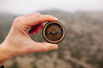 A person's hand holds a compass against the background of mountains or forests