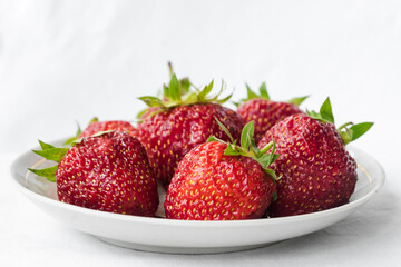 Red ripe strawberry in the white plate, light background. Plate with strawberries on white fabric. Summer vitamin berries juicy strawberry with strawberry leaf. Healthy eating and food concept