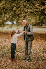 Fototapeta premium Grandfather spending time with his granddaughter in park on autumn day