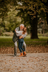 Grandfather spending time with his granddaughter in park on autumn day