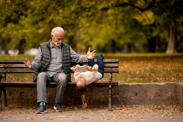 Grandfather spending time with his granddaughter on bench in park on autumn day