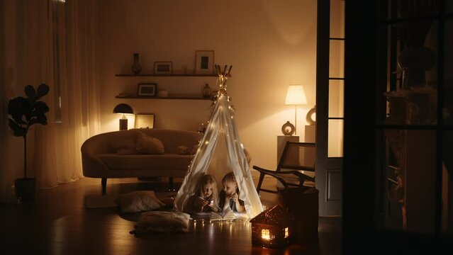 Happy family. Two children girl and boy are reading book in tent. Flashlight in hands of brother and sister. Happy family with book in tent. Children holds. reading book in selfmade house at bedroom