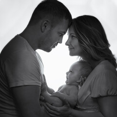 Black and white photography of happy family with infant son by the window. Smiling Newborn baby in arms mom and dad. Concept of love, protection of children.