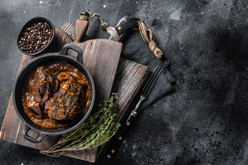 Stewed beef cheeks with brown red wine sauce in skillet. Black background. Top view. Copy space
