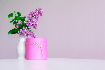 Bouquet of lilacs in a white vase and gift box on a light background. Copy space