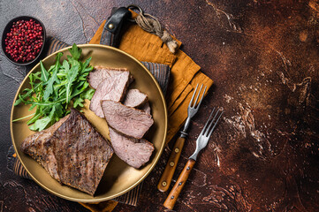 Roast Tri Tip or sirloin bottom beef steak on a plate with arugula. Dark background. Top view. Copy...
