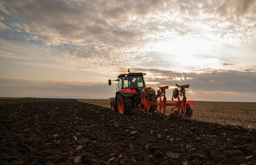 Fototapeta premium Tractor on the field during sunset.