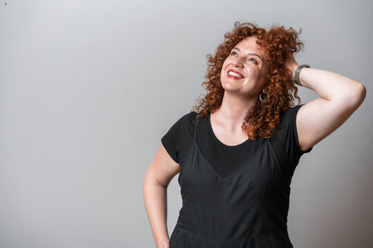 Happy woman with red curly hair posing on grey background
