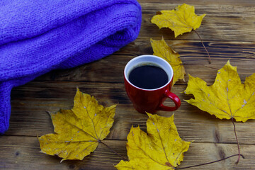 Cosy knitted blue sweater, cup of coffee and autumn maple leaves on wooden table. Autumn cozy concept
