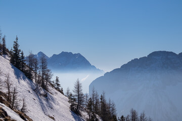 Scenic view on snow capped mountain peaks of Karawanks in Carinthia, Austria. Julian Alps. Winter wonderland in Austrian Alps, Europe. Ski tour, snow shoe hiking. Tiny trees on slope. Blue misty hills