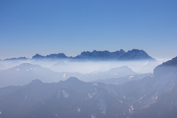 Fototapeta premium Scenic view from summit of Freiberg on misty snow capped mountain peaks in Karawanks mountains, Carinthia, Austria. Winter wonderland on sunny day in Austrian Alps, Europe. Ski tour, snow shoe hiking