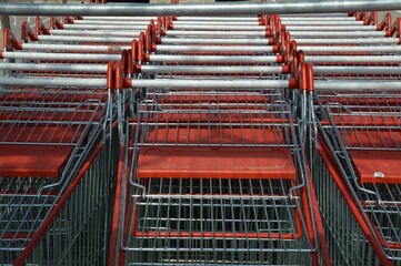 Closeup of rows of stacked metal shopping trolley carts with red handles
