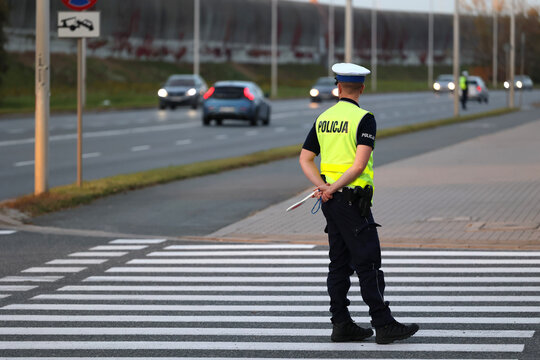 Policjant ruchu drogowego na przejściu dla pieszych kontroluje ruch pieszych. Przy radiowozie. 
