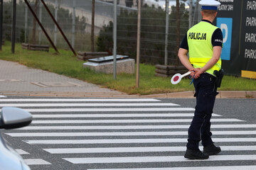 Policjant ruchu drogowego na przejściu dla pieszych kontroluje ruch pieszych. Przy radiowozie.  - obrazy, fototapety, plakaty