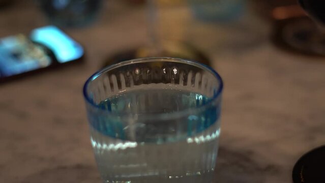 Vaso de agua de cristal azulado encima de una mesa con sobras diversas