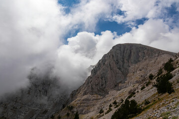 Fototapeta na wymiar Panoramic view of the cloud covered slopes and rocky ridges of Pieria Mountains near Mount Olympus in Mt Olympus National Park, Thessaly, Greece, Europe. Trekking on hiking trail through mystical fog