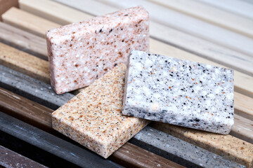 Porcelain three stoneware square samples laid on kitchen countertop examples of future kitchen fasade exterior. Samples slabs of natural granite marble quartz for stone countertops close up.
