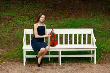 a girl with a violin sits on a white park bench