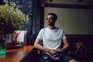 African american man in a white t-shirt sits in a coffee shop. Mock-up.
