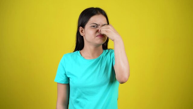Portrait of young woman pinching nose with disgust on his face due to bad smell isolated over yellow background