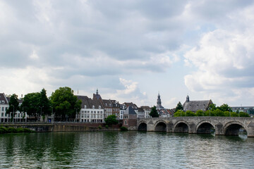 Fototapeta na wymiar urban cityscape off the city Maastricht in the netherlands, clouded sky. Skyline with river in the front and stone bridge on the right. Travel destination european culture historic architecture. 