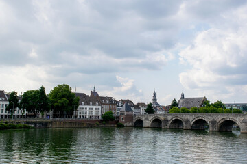 urban cityscape off the city Maastricht in the netherlands, clouded sky. Skyline with river in the front and stone bridge on the right. Travel destination european culture historic architecture. 