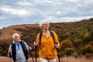 Active senior couple with backpacks hiking together in nature on autumn day.
