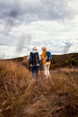 Naklejka na ściany i meble Rear view of active senior couple with backpacks hiking together in nature on autumn day.