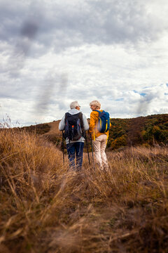 Rear view of active senior couple with backpacks hiking together in nature on autumn day.