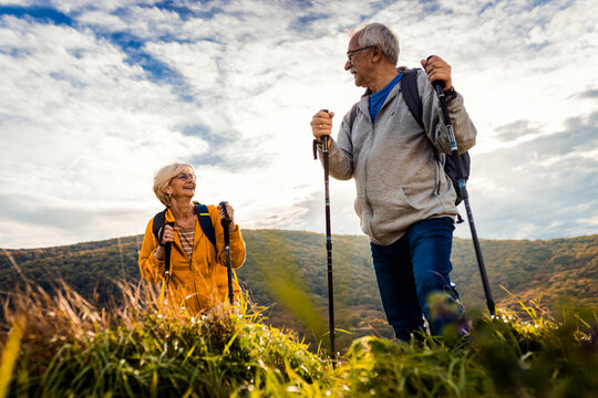 Active senior couple with backpacks hiking together in nature on autumn day.