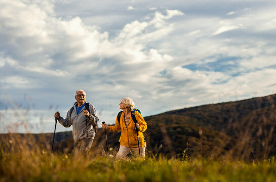 Active senior couple with backpacks hiking together in nature on autumn day.