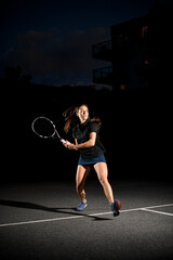 Fototapeta na wymiar Great view on active woman with racket playing tennis on outdoor court at evening.