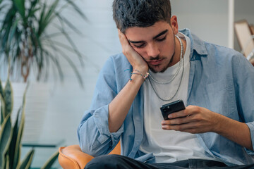 young man at home looking at mobile phone bored