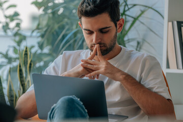 young man at home with laptop thinking or deciding