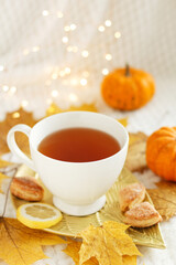 Obraz na płótnie Canvas Creative mood. A cup of tea with lemon, cookies, autumn leaves and pumpkin on a white plaid with lights. Cozy autumn composition. Autumn mood concept.