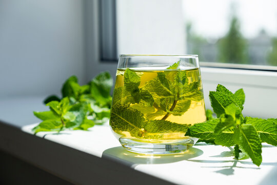 Glass with mint tea on window sill and fresh mint leaves around. Herbal tea. Moroccan tea with mint.
