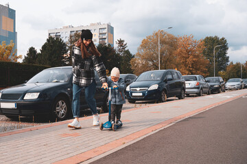 Mother and son having fun. Happy family mother teaches child son to ride a scooter in the city street. Support childhood parenthood idea. happy family concept