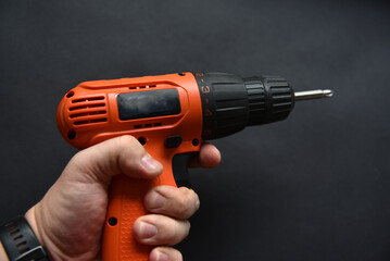 Orange screwdriver on a black background in the hand. Screwdriver and electric drill with power supply