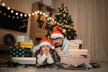Bearded young caucasian father lying on floor with his cute preschooler daughter with gifts in...