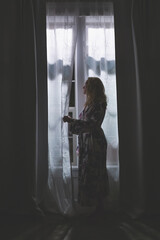 Silhouette of woman looking out window through curtains at nighttime in the dark