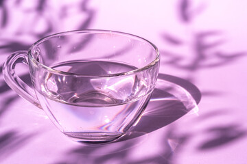 Abstract shadow pattern on a pink background and glass cup with water. Texture for the background.