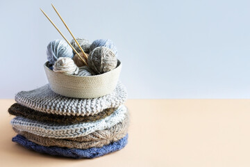 Gray, brown and blue balls of knitting threads in a beige basket with bamboo knitting needles and a stack of knitted hats for winter and autumn, knitting hobby