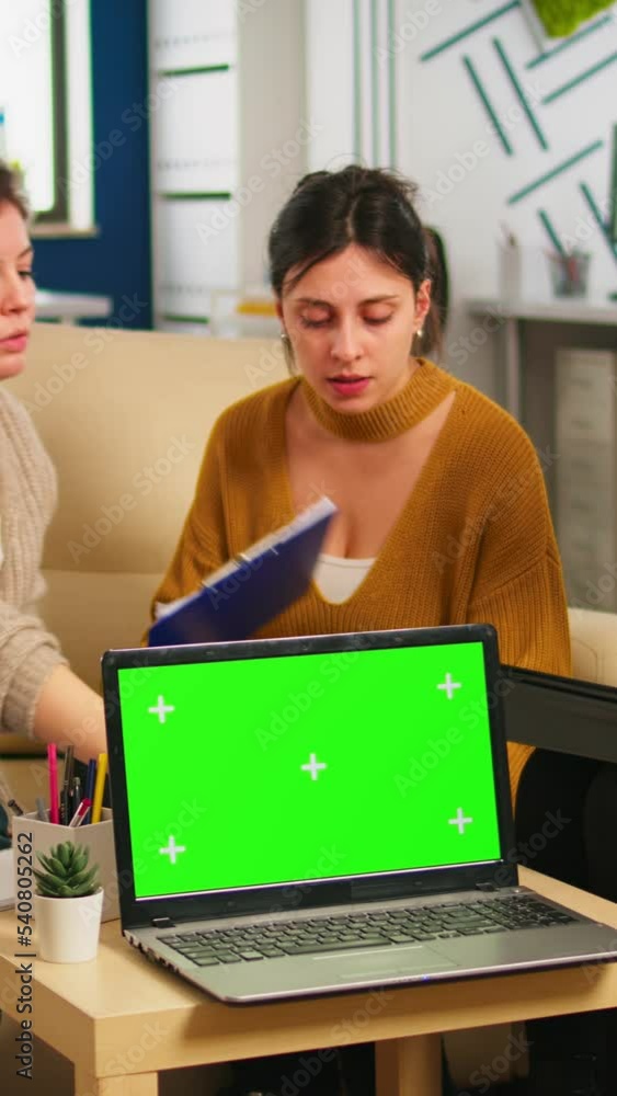 Poster diverse women sitting at table in start up office discussing strategy with green screen laptop in fr