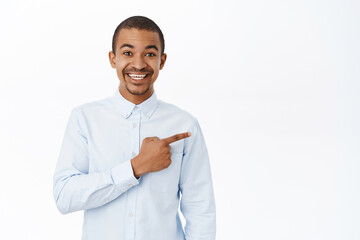 Smiling handsome man pointing right, showing direction, demonstarting promo, standing over white background