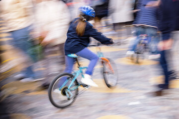 Fototapeta na wymiar motion blur picture of a young unrecognizable girl with a bicycle between crowds of people