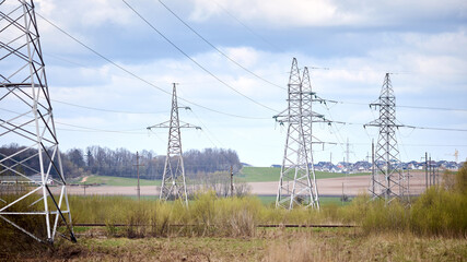 High voltage electric high voltage electric transmission power towers with electric glass insulator over cloudy stormy dark sky near spring landscape field railway and village 16x9 panoramic shot.