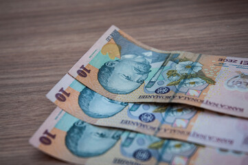 Ten Romanian Leu banknotes on brown background.